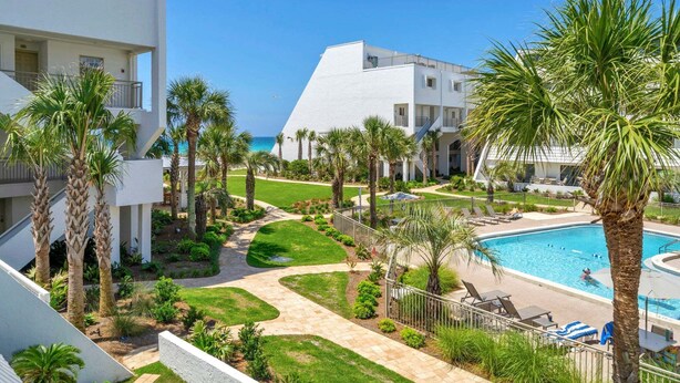 A resort with a swimming pool, palm trees, and a view of the ocean. - Aegean 215 – Updated Condo with Private Balcony & Beach Access (Destin)