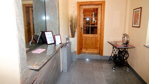 A reception area with a marble counter, a wooden door, a sewing machine on a table, and a framed certificate on the counter. - Messe-Hotel Waldruhe (Giesen)