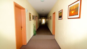 A hallway with doors on both sides, framed pictures on the walls, and a carpeted floor. - Messe-Hotel Waldruhe (Giesen)