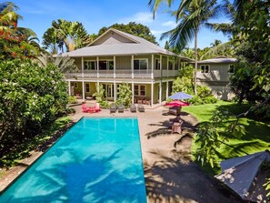 Ein zweistöckiges Haus mit Swimmingpool, umgeben von üppiger Vegetation und Palmen.