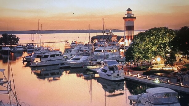 A marina with multiple yachts docked, a lighthouse in the background, and a tree-lined dock area. - BEST VALUE ON THE BEACH IN SEA PINES!
ALMOST OCEANFRONT! (Hilton Head Island)