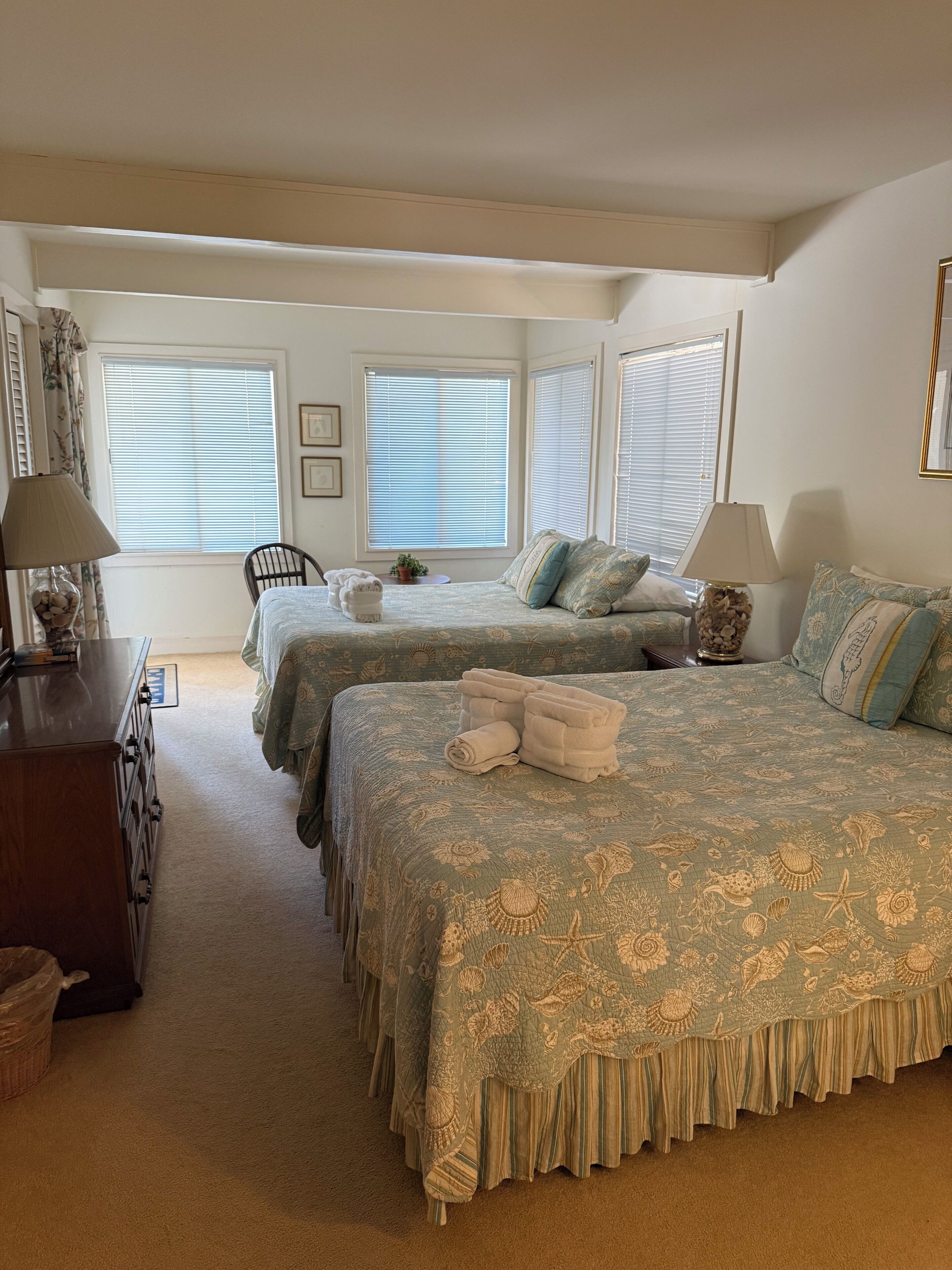 A bedroom with two beds, a dresser, and a chair.