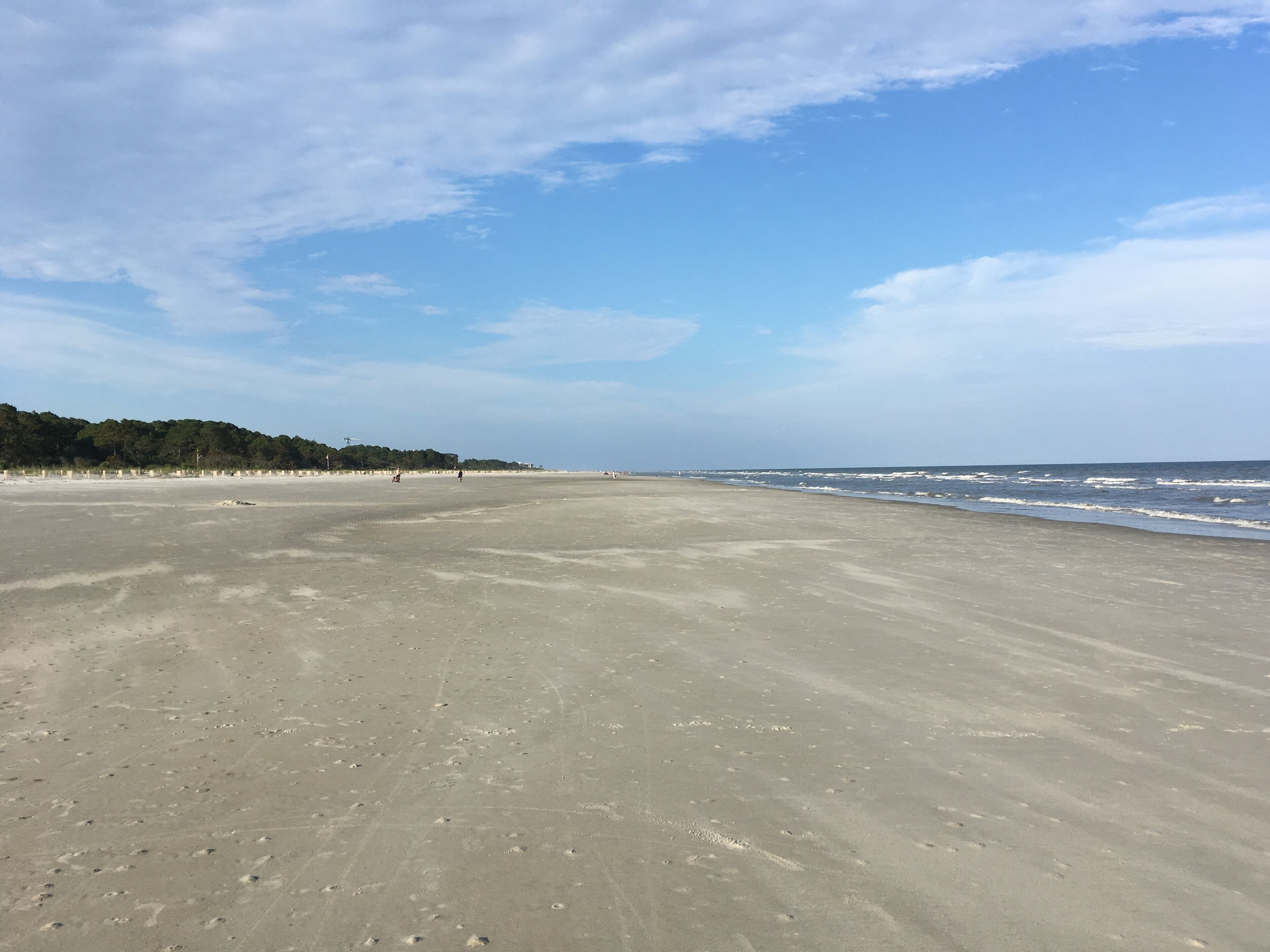 A wide, sandy beach with gentle waves and a clear sky.