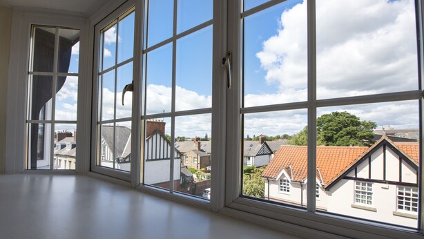 Et værelse med store vinduer der giver udsigt til omkringliggende huse og en klar himmel.