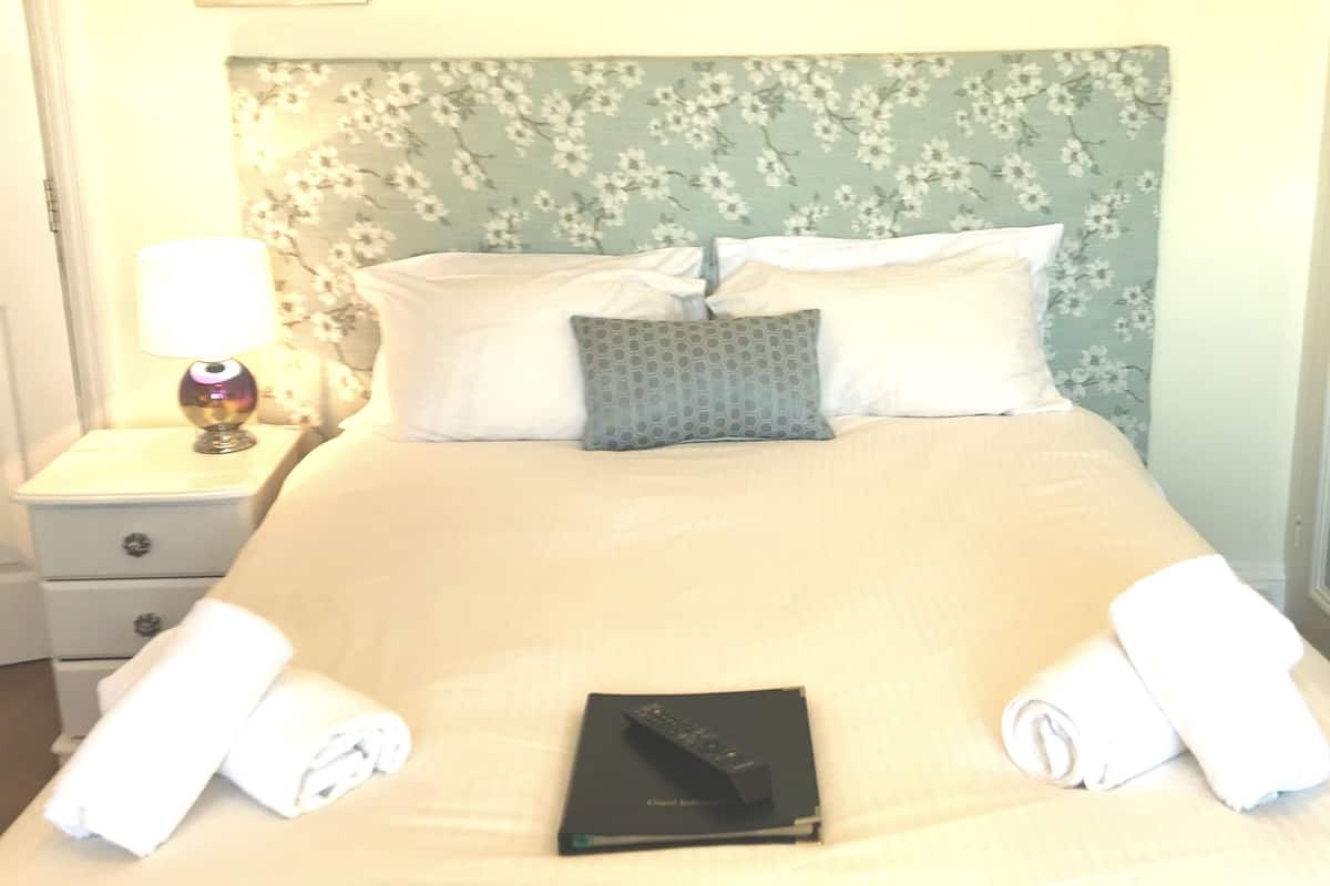 A neatly made bed with a floral headboard, a bedside lamp, and a book on the bed.