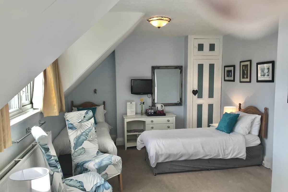 A bedroom with a bed, a chair, a desk, a mirror, and a TV.