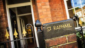 A metal gate with a sign reading "St Raphael" and a brick wall in the background.