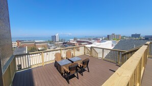 Um deck de madeira com mesa e cadeiras, com vista para um horizonte urbano e um corpo d'água.
