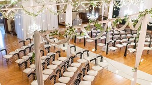 Espaço para casamento com fileiras de cadeiras, cortinas brancas e luzes de cordão.