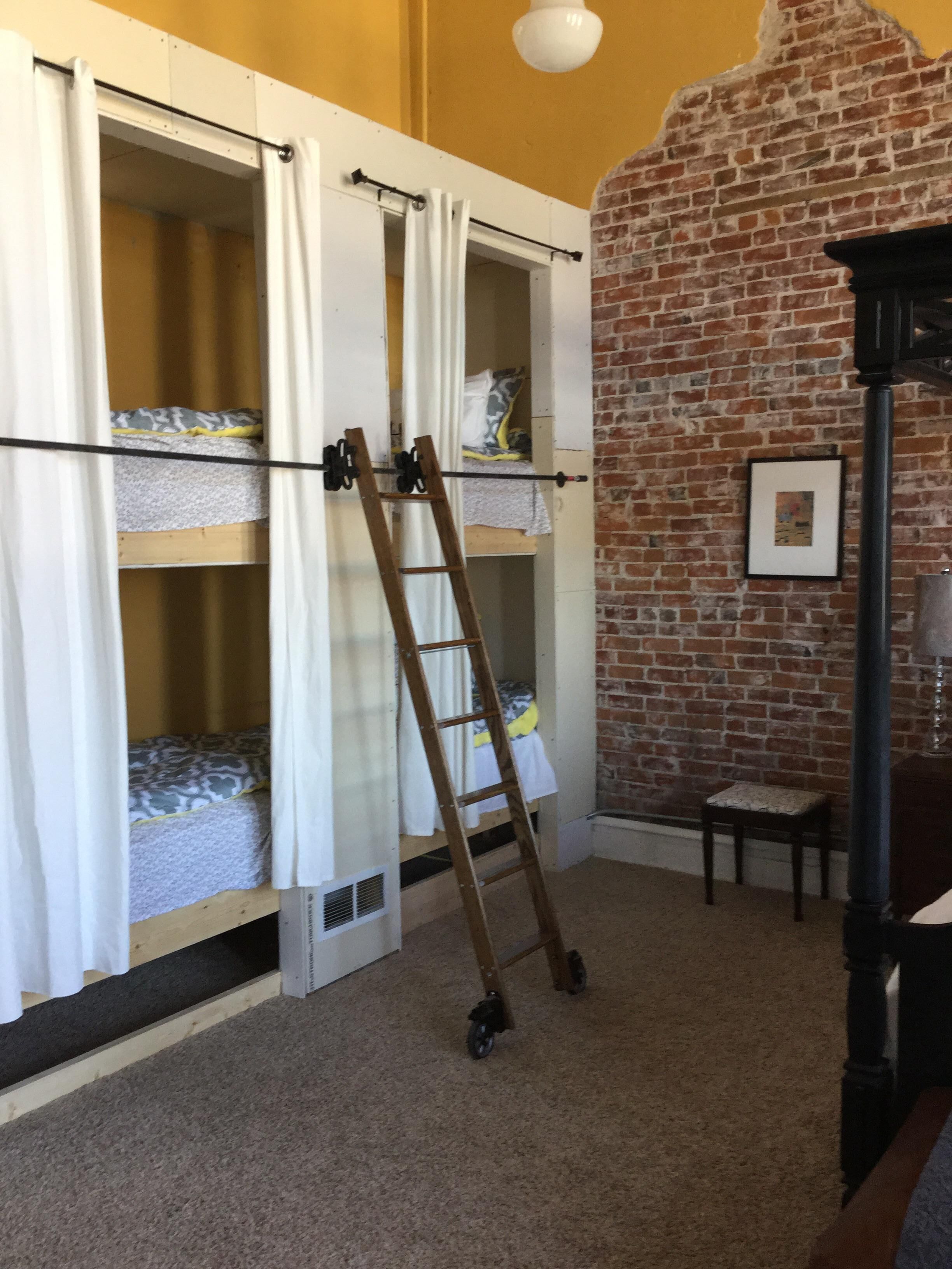 A room with bunk beds, a ladder, a brick wall, and a small table.