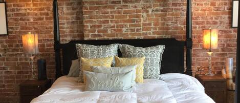 A four-poster bed with a brick wall backdrop, a wooden headboard, and multiple pillows.