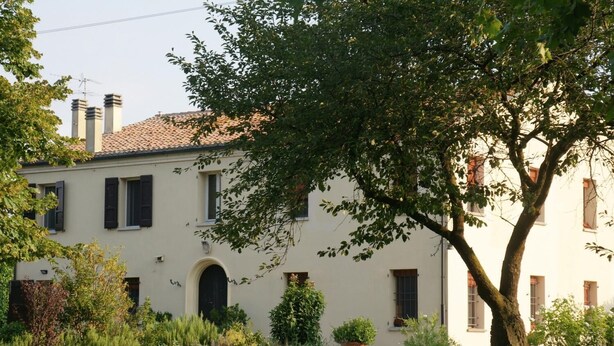 A two-story building with a tiled roof, multiple windows with shutters, and a well-maintained garden with various plants and a large tree. - Alla Cedrara agriturismo (Ferrara)