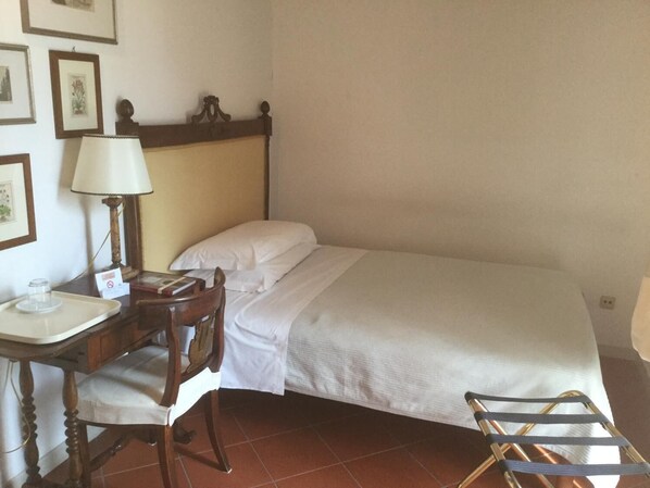 A small, neatly arranged bedroom with a single bed, a wooden chair, a desk with a lamp, and a small table with a tray. - Alla Cedrara agriturismo (Ferrara)