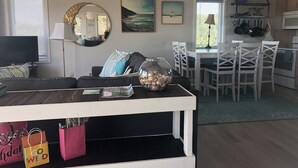 A living room with a sofa, TV, and a dining area with chairs and a table. - Sunset Dream - sunset view, short walk to beach (Surf City)