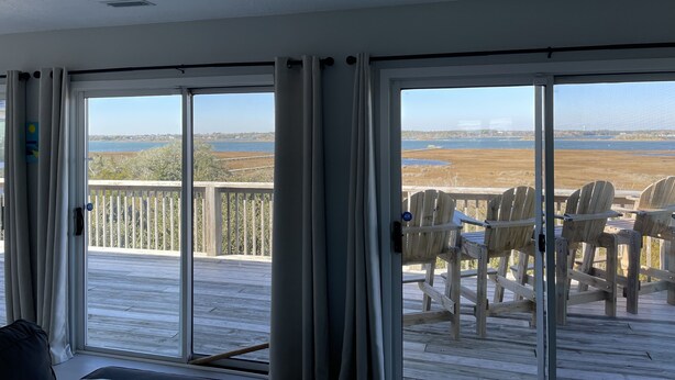 A room with a large sliding glass door leading to a wooden deck with outdoor chairs. - Sunset Dream - sunset view, short walk to beach (Surf City)