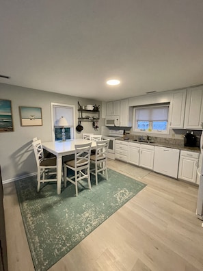 A kitchen with white cabinets, a dining table with chairs, a microwave, and a stove. - Sunset Dream - sunset view, short walk to beach (Surf City)