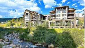 Un hôtel à plusieurs étages, doté de balcons, qui se dresse sur un site offrant une vue imprenable sur les montagnes et une rivière sinueuse.