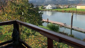 A riverside view with a wooden dock, a statue, and houses in the background.