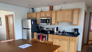 A compact kitchen with wooden cabinets, a stainless steel refrigerator, a microwave, a stove, and a sink.