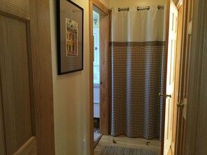 A hallway with a wooden door, a framed picture on the wall, and a shower curtain with a checkered pattern. - Charming Cottage in Maine (Surry)