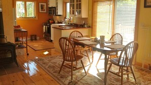 Una cocina amplia con armarios de madera, un comedor con mesa y sillas, y un gran ventanal con persianas.