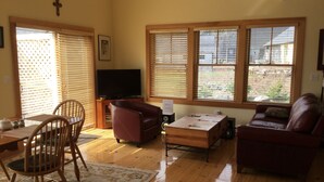 Una sala de estar con piso de madera, televisor, sofá y zona de comedor con sillas y una mesa.