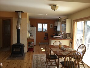 A cozy living room with a fireplace, wooden flooring, and a dining area with chairs and a table. - Charming Cottage in Maine (Surry)