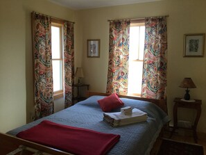 A bedroom with a bed, a nightstand, a lamp, and a window with curtains. - Charming Cottage in Maine (Surry)