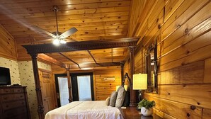 A wooden cabin bedroom with a bed, dresser, lamp, and ceiling fan.