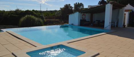 Una piscina con zona hundida, rodeada por una solería alicatada y un área de estar cubierta con un flotador visible.