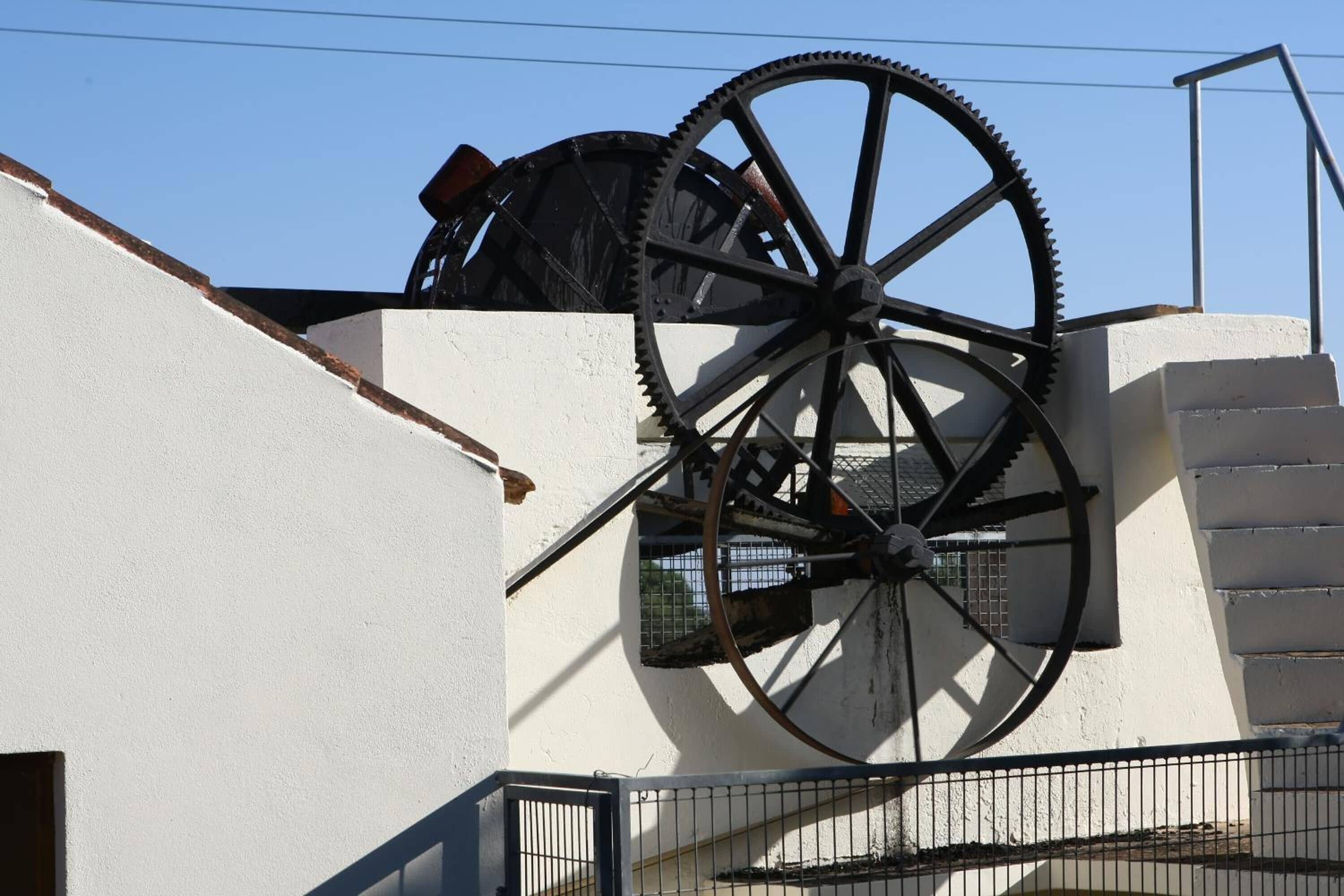 Un edificio con ruedas metálicas grandes y oxidadas a la vista, lo que sugiere una característica histórica o industrial.
