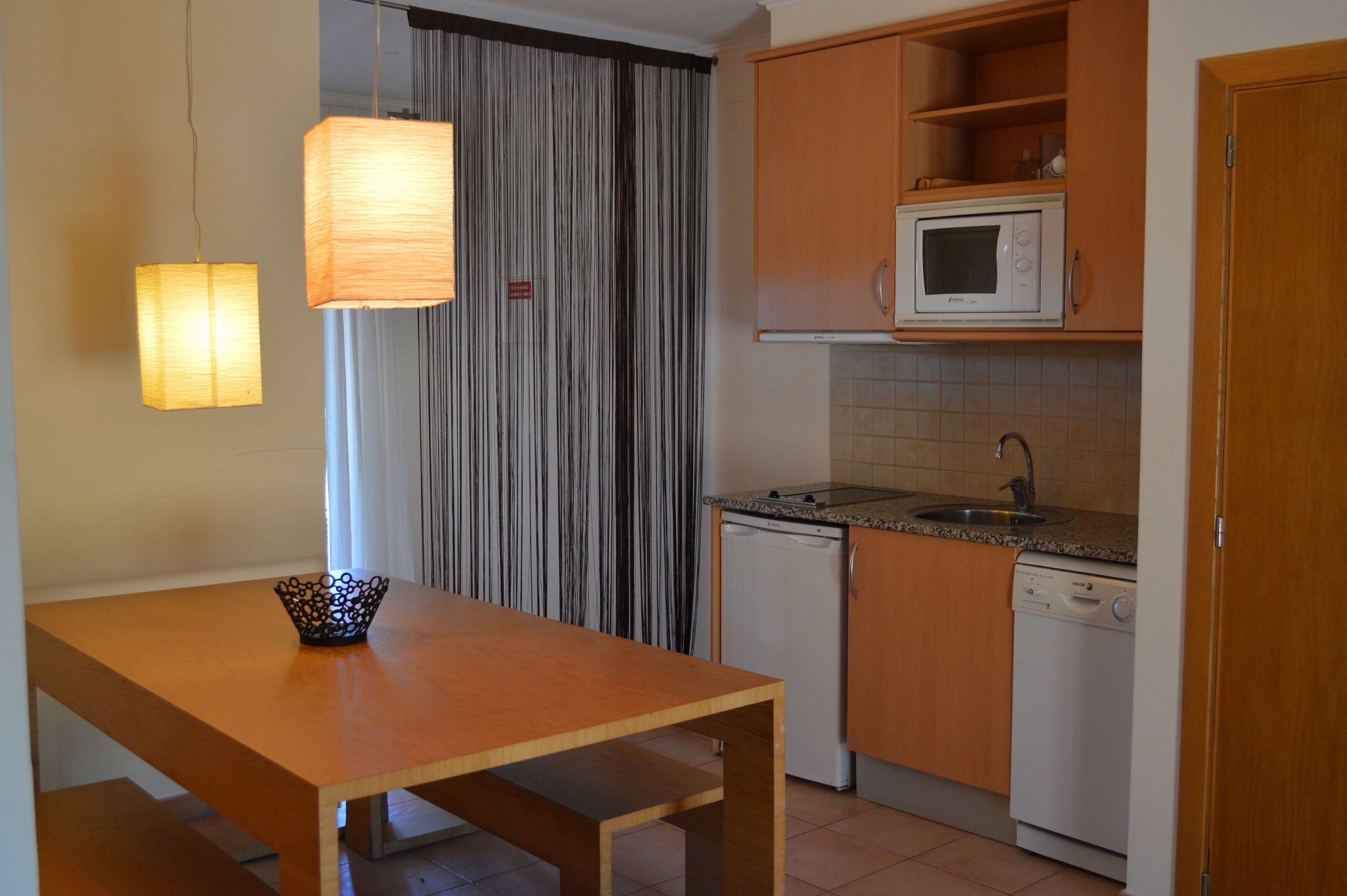 A compact kitchen with a wooden table, a microwave, a dishwasher, and a curtain.