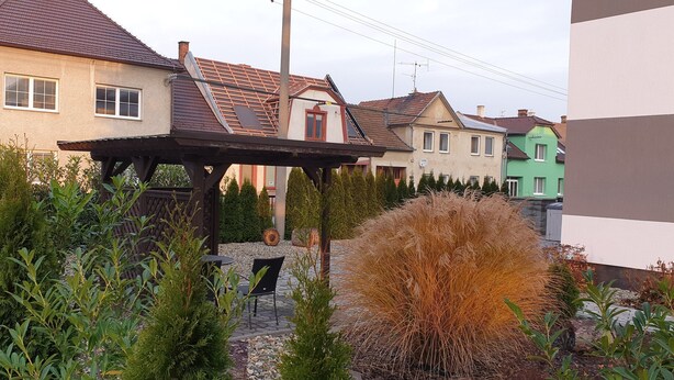 A residential area with houses, a garden with plants and a pergola, and a clear sky. - Apartma Transpet (Kostelec na Hané)