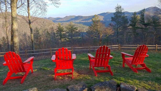 Drie rode Adirondack-stoelen gericht op een bergachtig landschap, met een houten hek op de achtergrond.