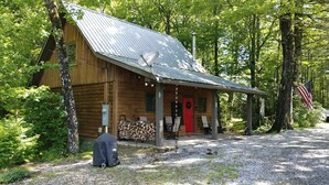 Een houten hut met een metalen dak, een veranda met stoelen en een stapelhout.
