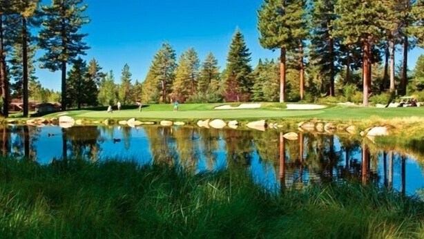 Un campo de golf con un estanque, árboles y cielo despejado.