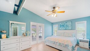 Ein Schlafzimmer mit Bett, Deckenventilator, Kommode und Fenster mit Jalousien.