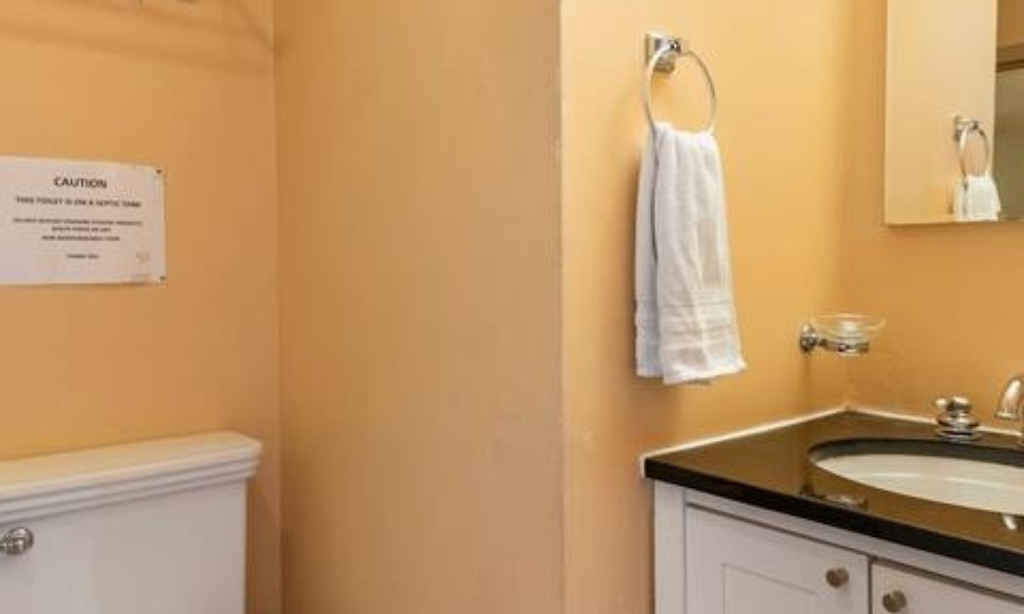 Une salle de bain équipée d’un lavabo, d’un miroir, d’un porte-serviettes et d’un panneau d’avertissement.