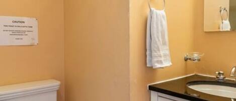 Une salle de bain équipée d’un lavabo, d’un miroir, d’un porte-serviettes et d’un panneau d’avertissement.