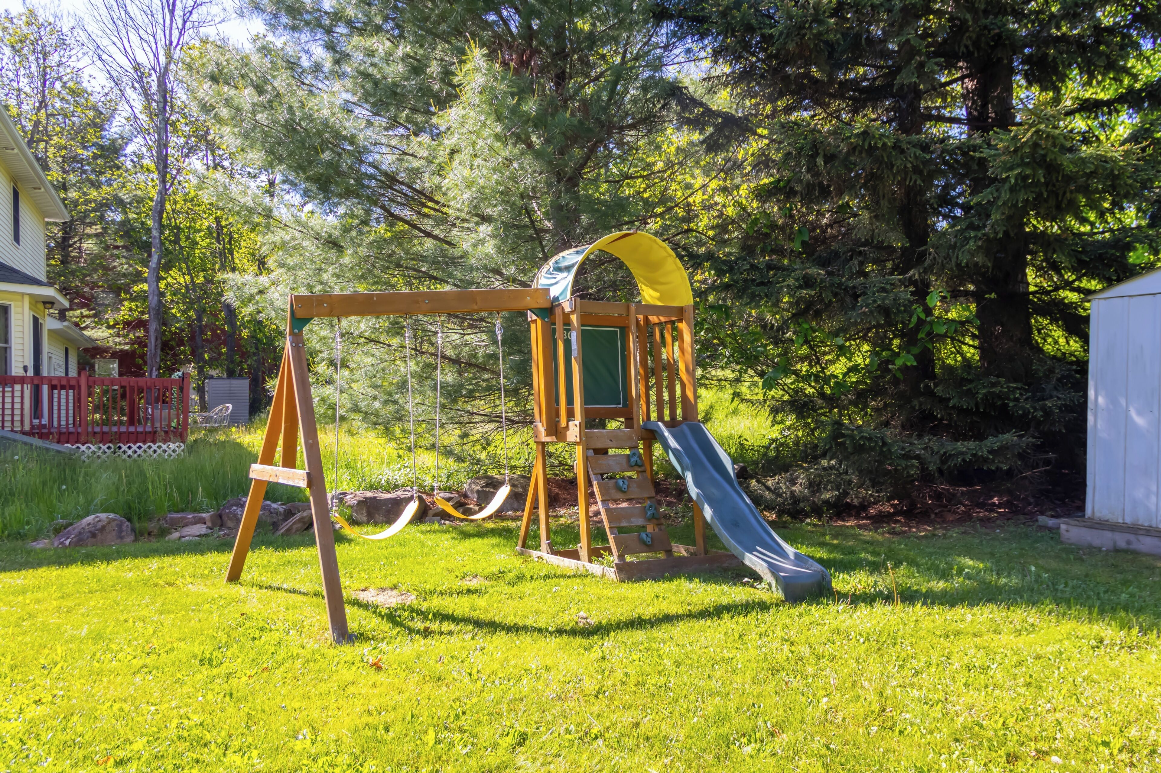 Une aire de jeux avec des balançoires et un toboggan, entourée d’herbe et d’arbres.