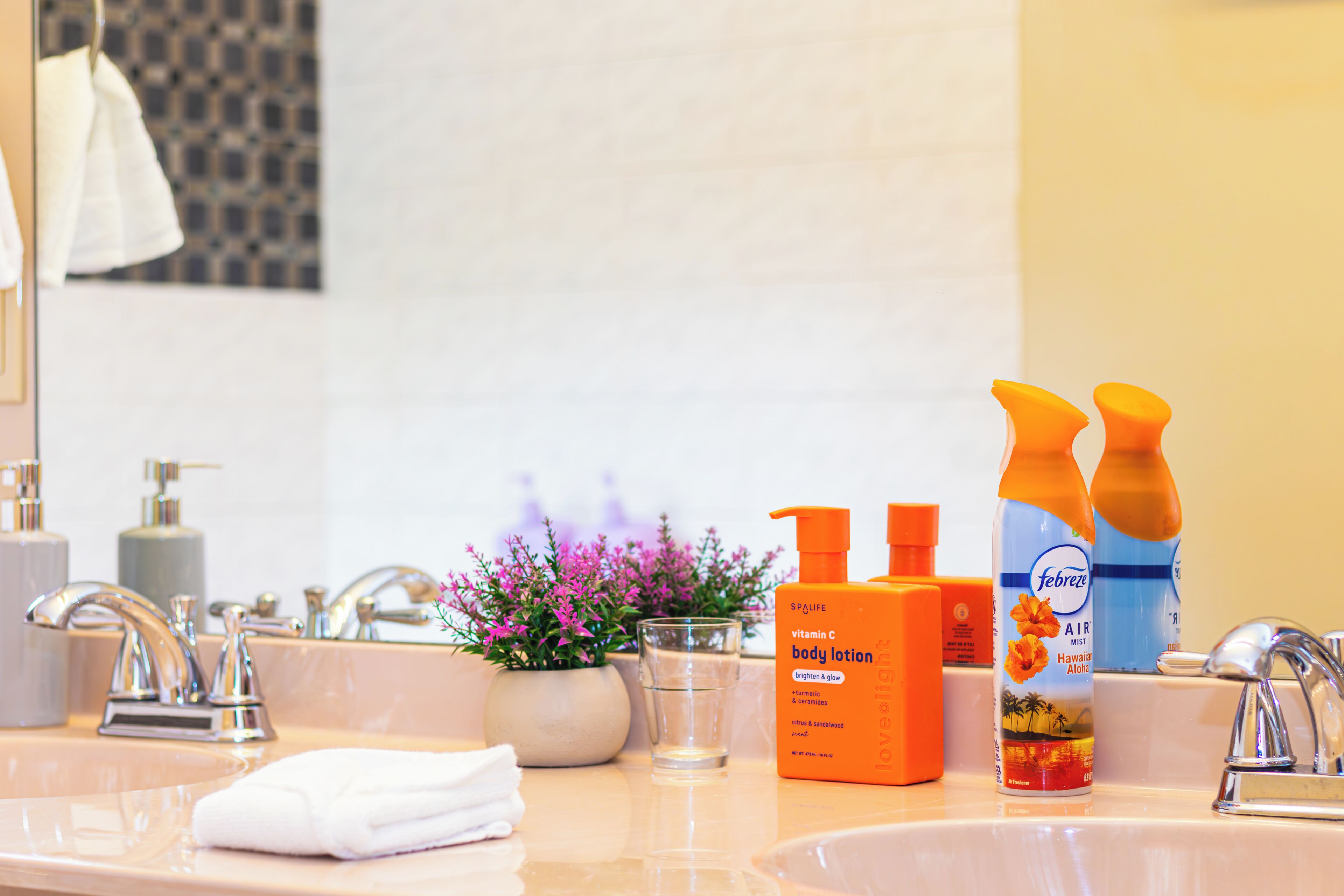 A bathroom with a sink, two bottles of body lotion, a glass of water, and a potted plant.