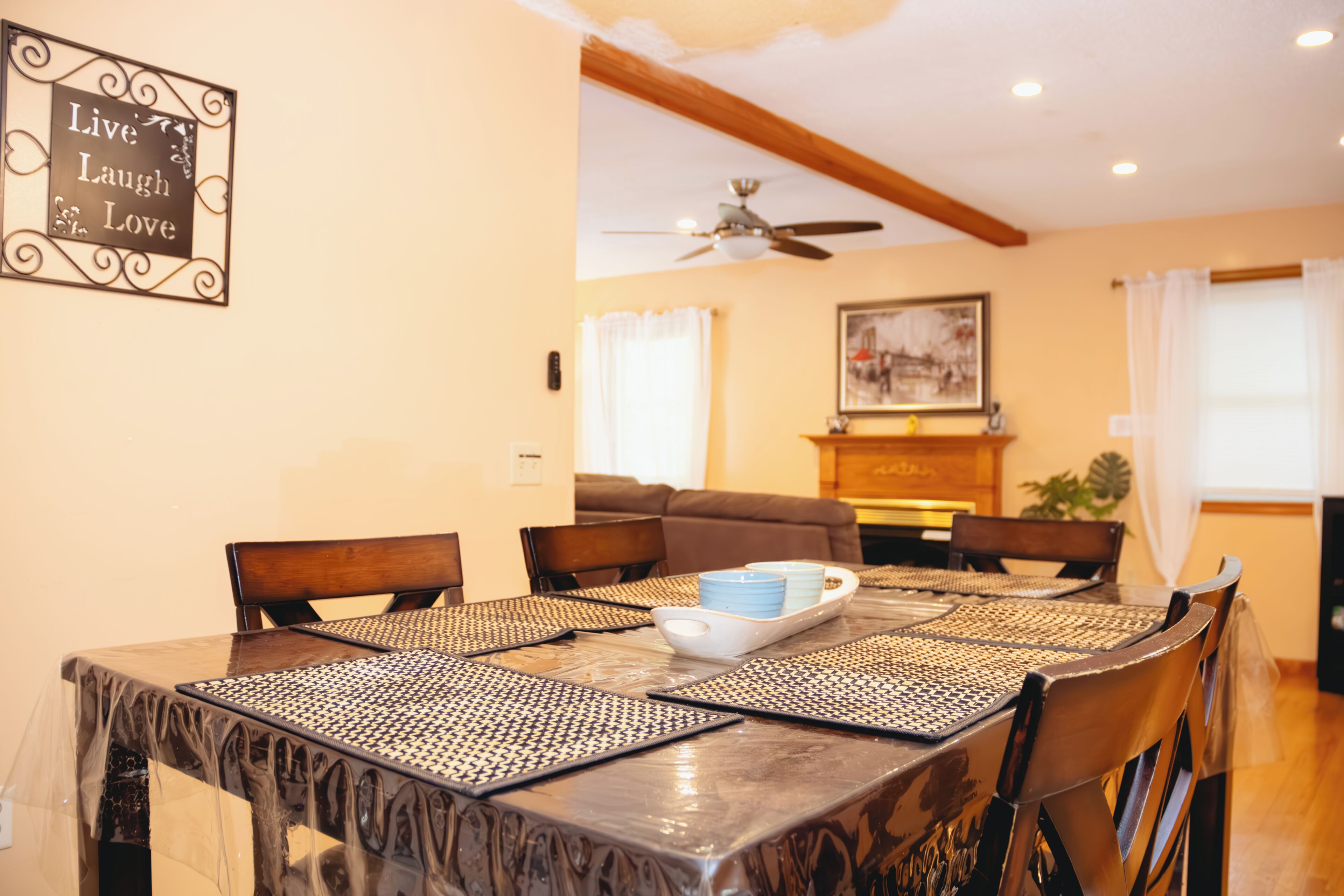 A dining area with a table set for four, a ceiling fan, and a painting on the wall.