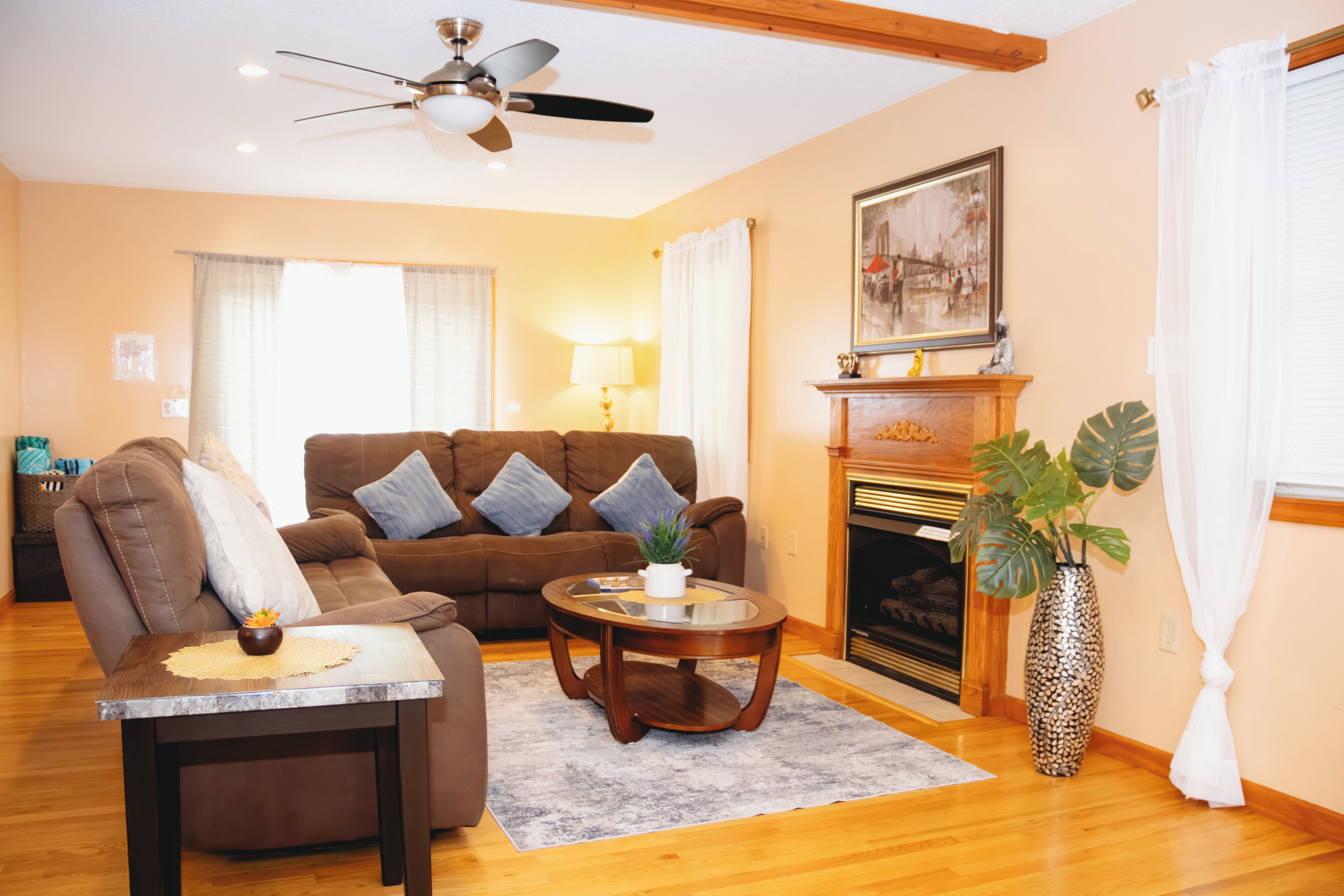 A living room with a brown sofa, a coffee table, a fireplace, and a ceiling fan.