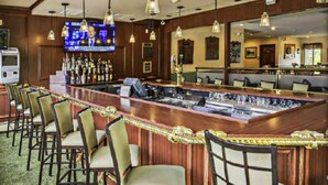 A bar area with a long counter, multiple bar stools, and hanging pendant lights.