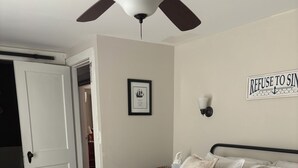 Een slaapkamer met een bed, een plafondventilator, een ingelijst schilderij en een bord aan de muur.