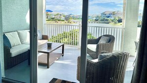 Ein Balkon mit Korbmöbeln, einem Tisch und Blick auf eine Wohngegend mit Häusern und einem Gewässer.