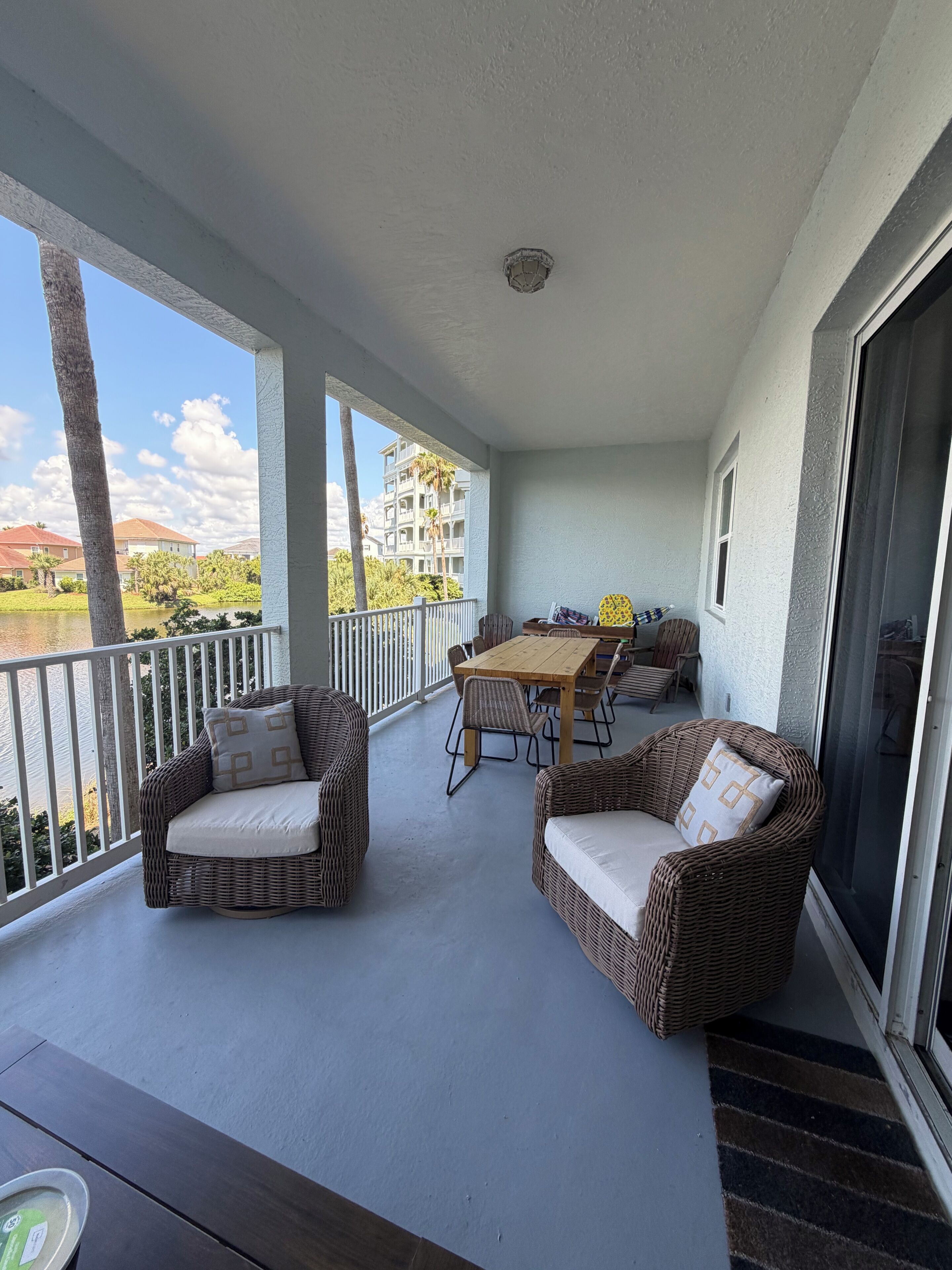 A balcony with wicker furniture, a wooden table, and a view of a building and trees.