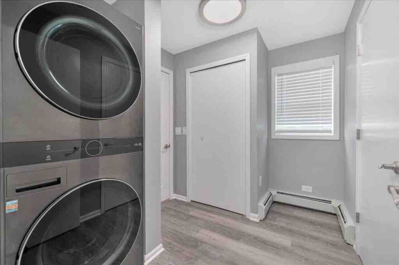 A laundry room with two washing machines, a door, and a window with blinds.