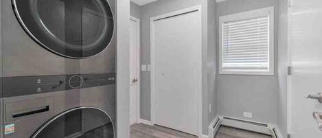 A laundry room with two washing machines, a door, and a window with blinds.