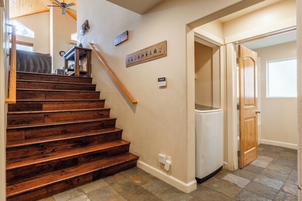 A staircase with wooden steps leading to a landing, a ceiling fan, a wall-mounted plaque, and a refrigerator in a hallway.